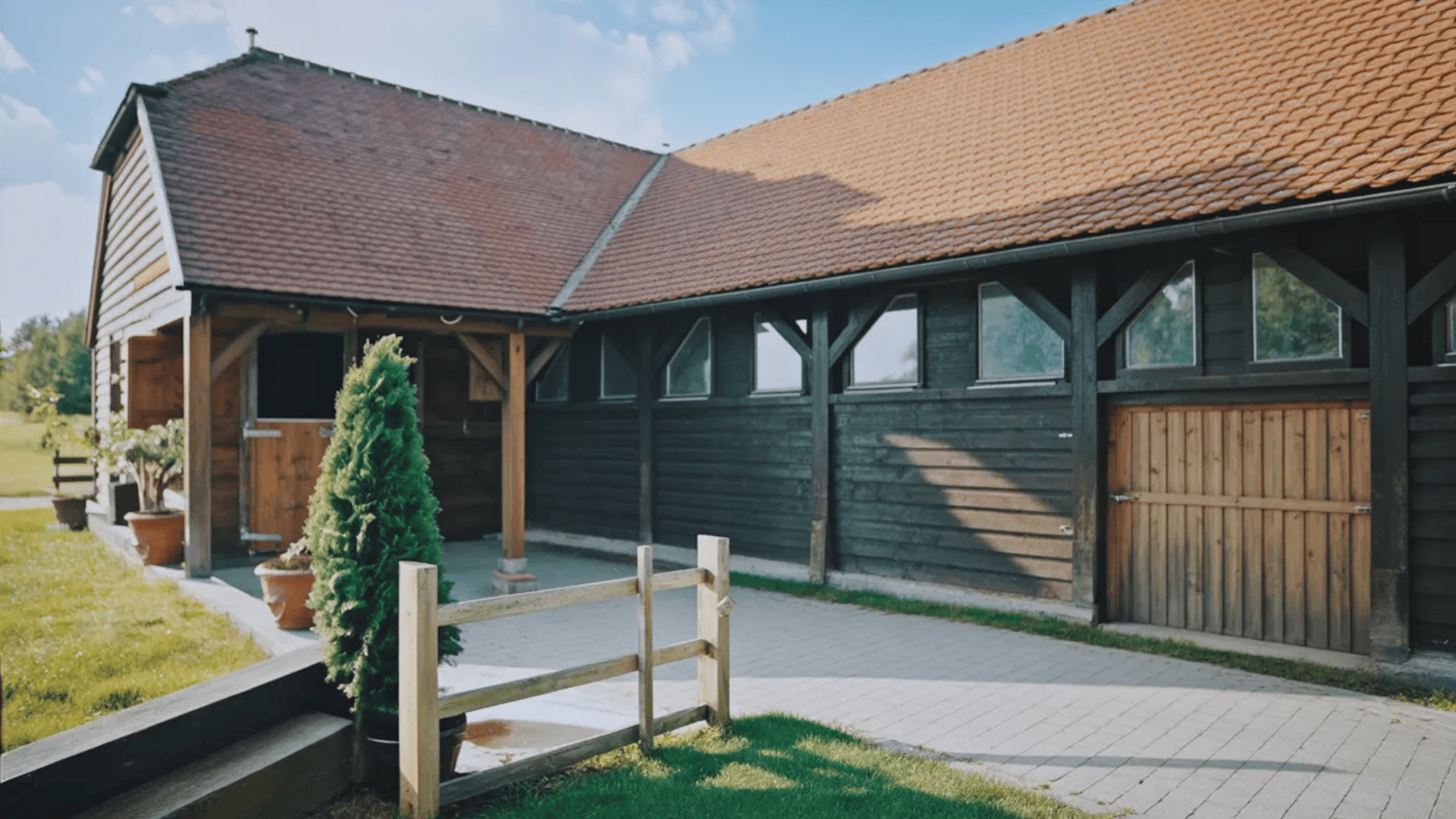 A rustic barn with wooden doors stands beside a wooden fence in a rural setting