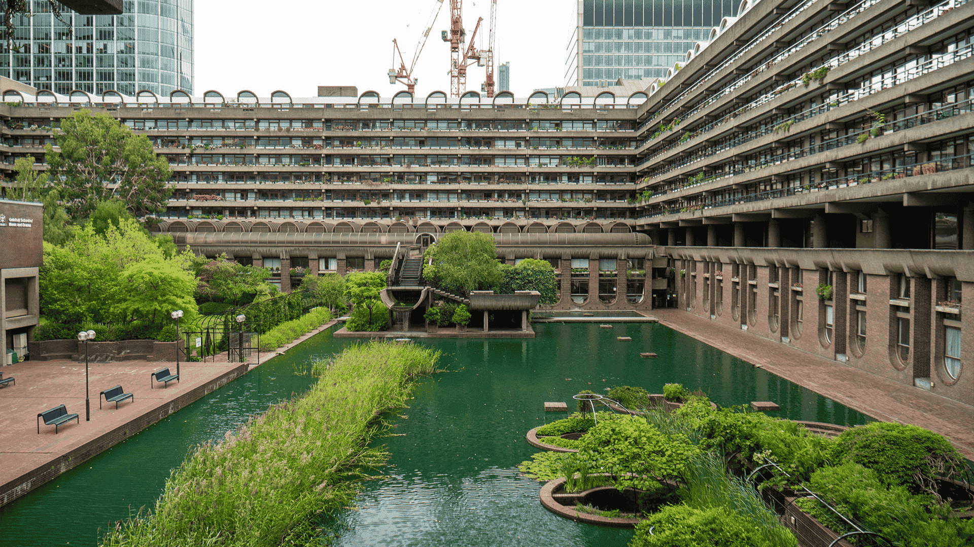 A serene courtyard featuring a pond surrounded by elegant buildings under a clear blue sky, which creates a clear view of the pond.