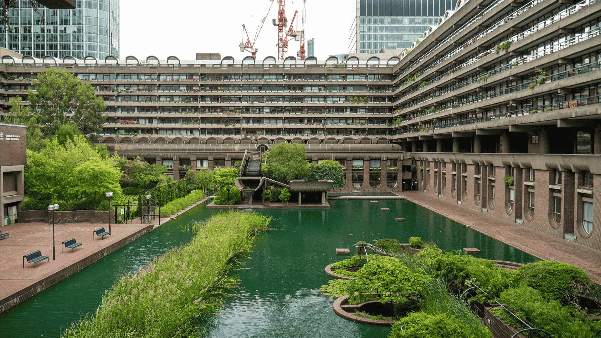A serene courtyard featuring a pond surrounded by elegant buildings under a clear blue sky, which creates a clear view of the pond.