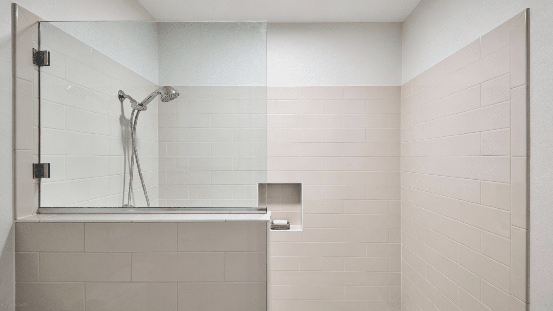 A small walk in shower with a tiled half wall and a clear glass top panel, featuring a built in niche and modern fixtures