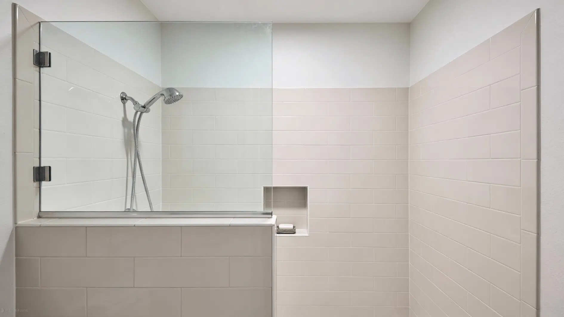 A small walk in shower with a tiled half wall and a clear glass top panel, featuring a built in niche and modern fixtures