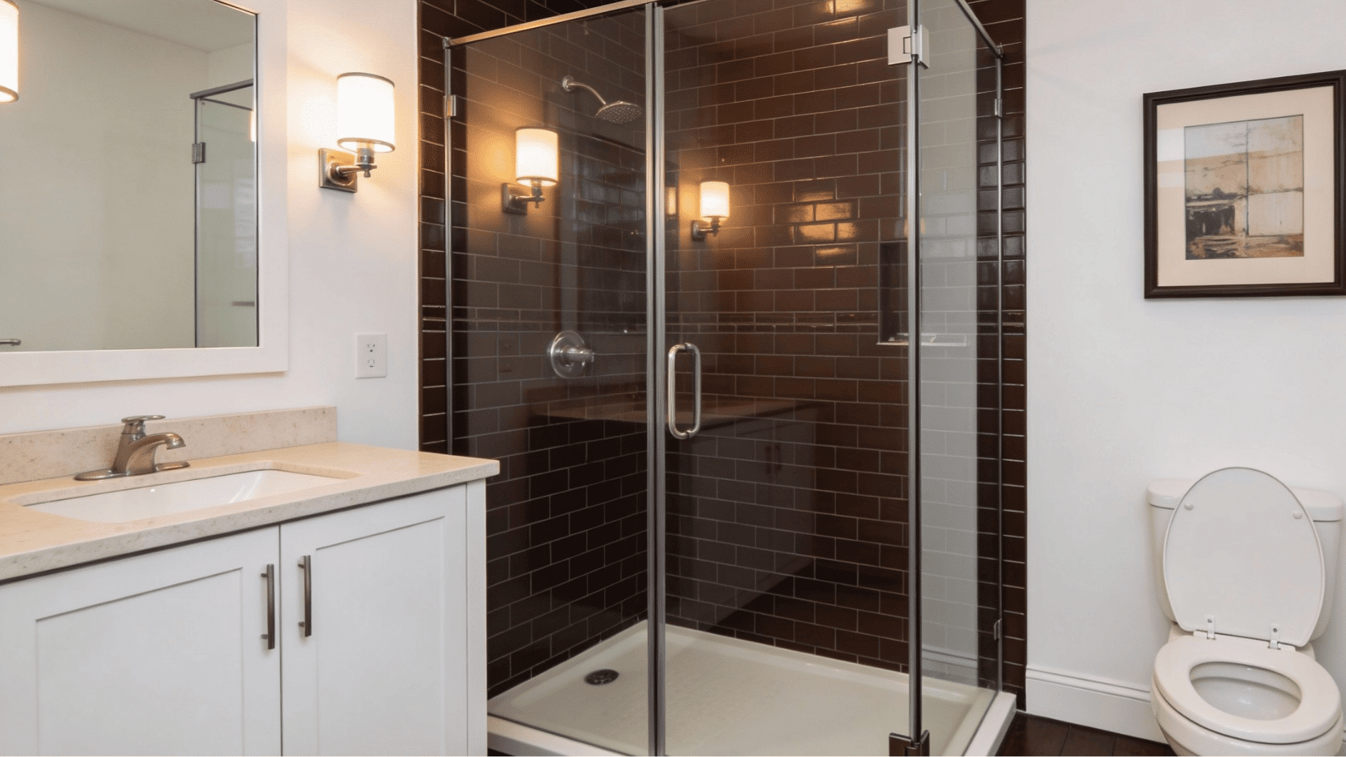 Alcove style walk in shower set between two walls, with a clear glass door, dark tile, bright vanity, and toilet beside it