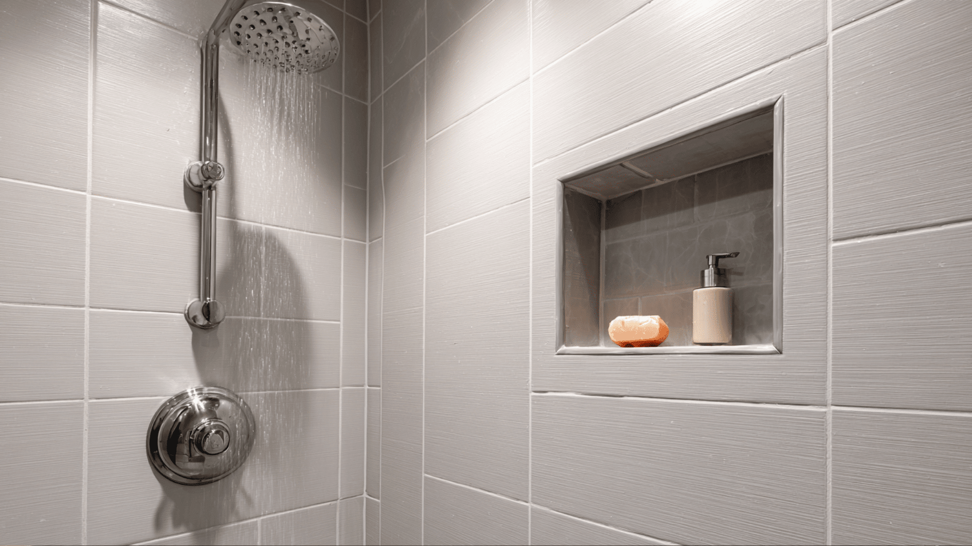 Modern tiled shower with a built in wall niche holding soap and candles, plus a chrome showerhead and control for a clean look