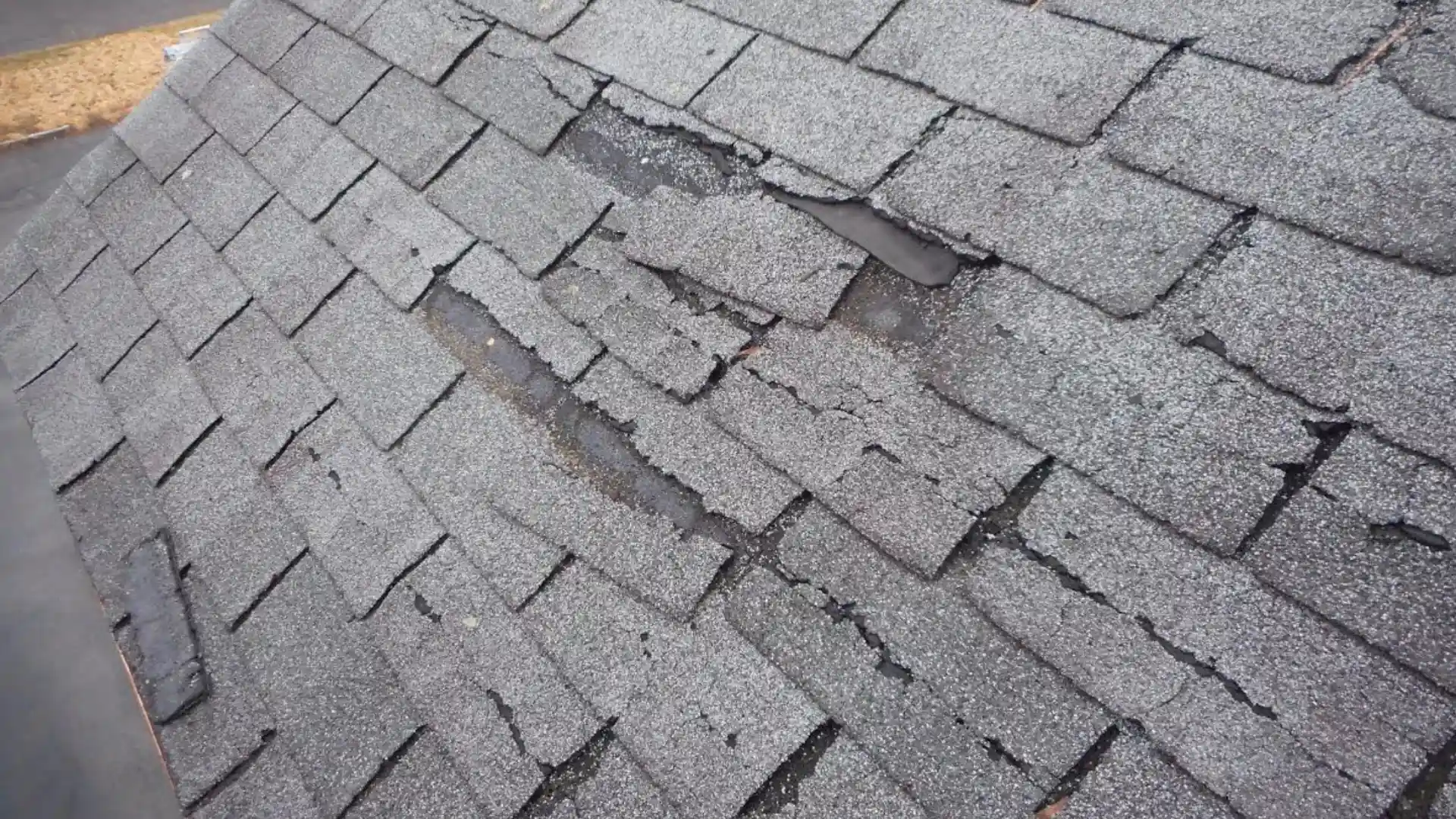 A damaged shingle roof showing a prominent crack in the roof and shingles, indicating potential structural issues