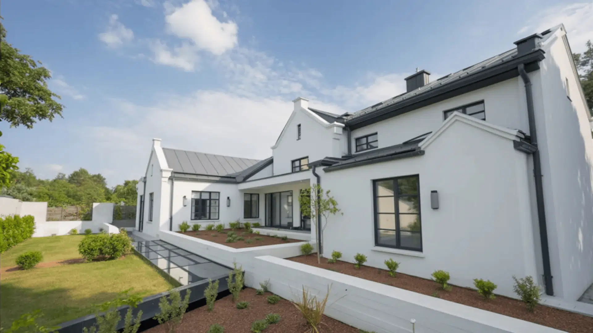 Large white brick house with black trim, sloped roof, wide yard, and clean modern landscaping