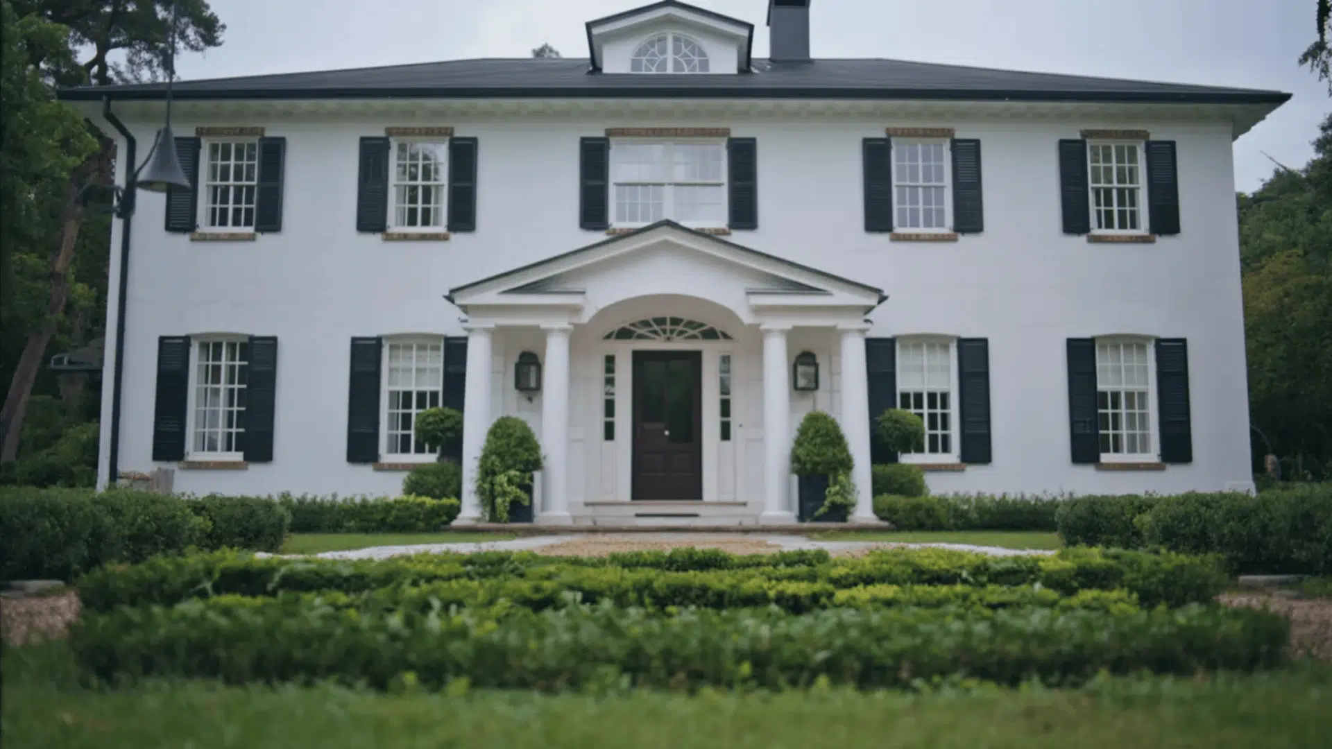 White brick colonial house with black shutters, central door, columns, and symmetrical front garden