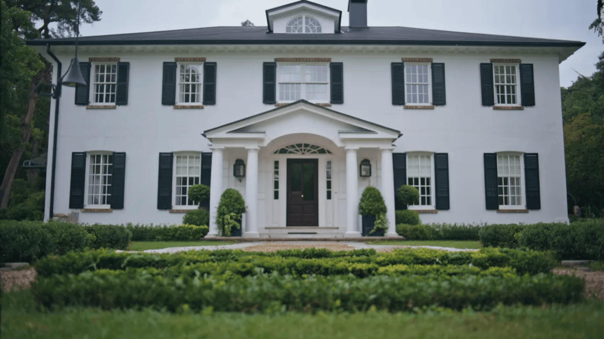 A white house featuring black shutters and a prominent front door, set against a clear blue sky