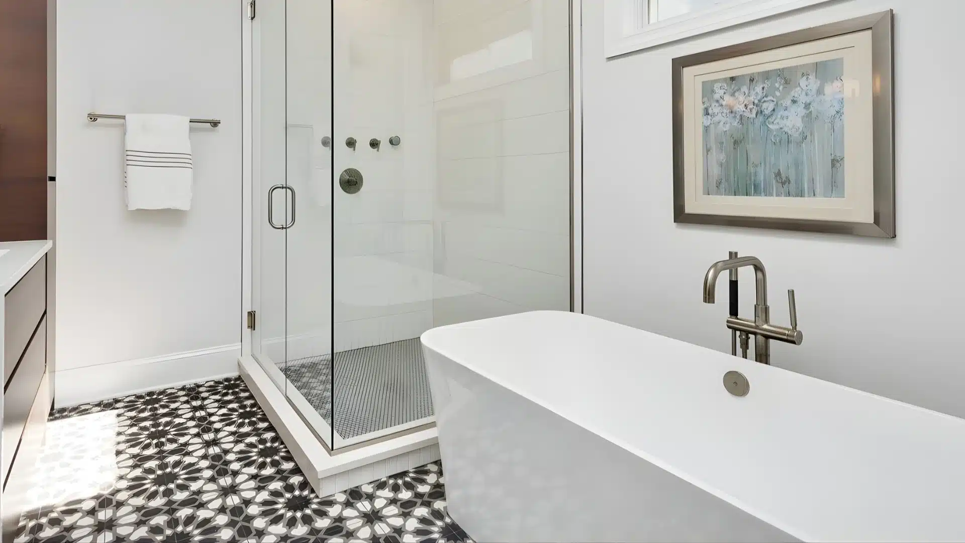 Modern bathroom featuring a freestanding white soaking tub, glass-enclosed shower, and black-and-white patterned mosaic floor tiles