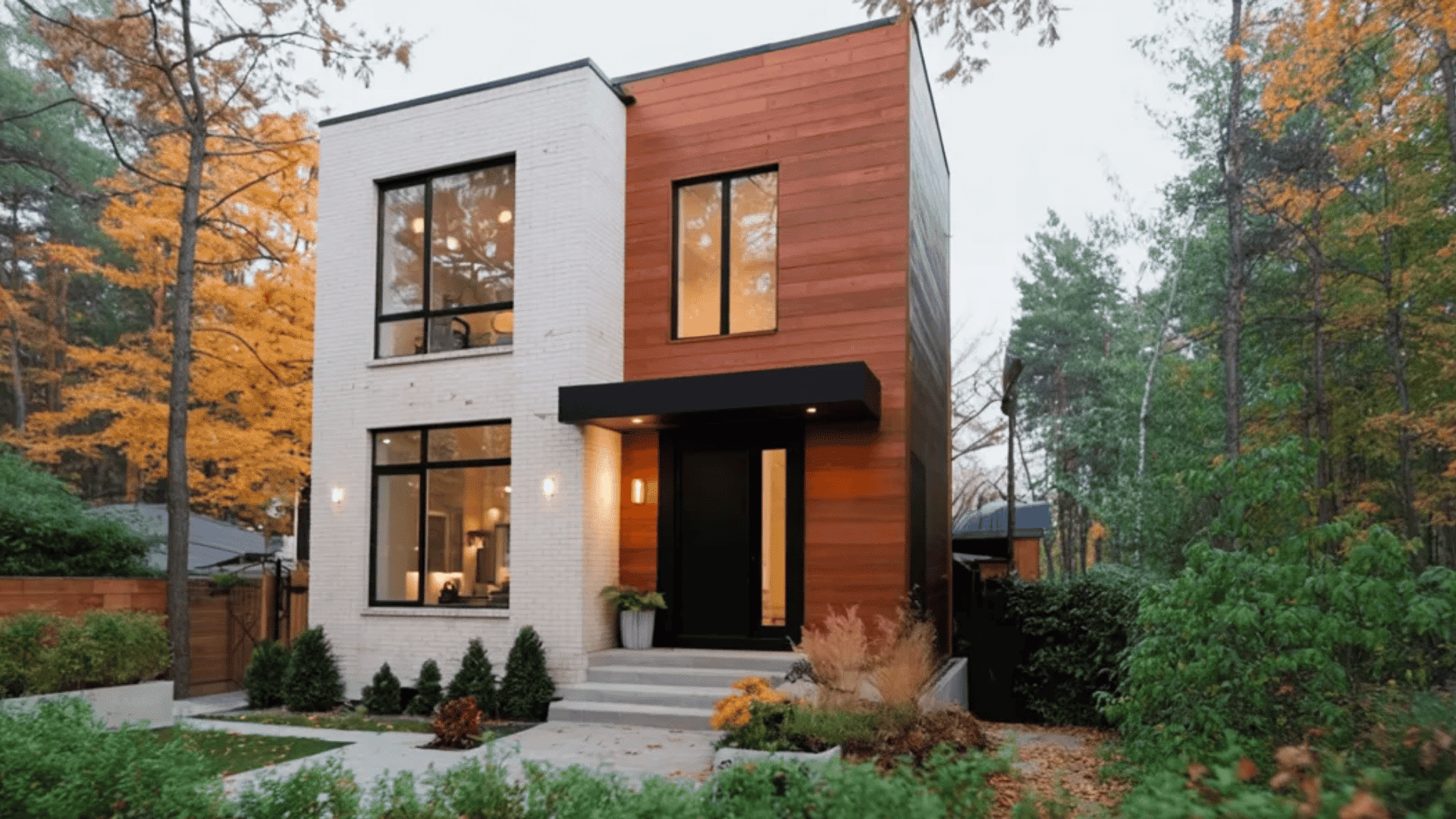 Modern white house with wood panel facade, black entry door, and trees with autumn leaves