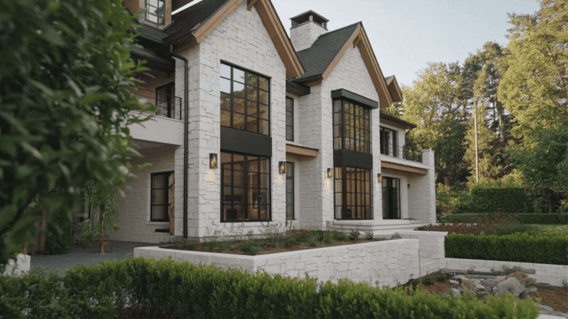 White house with large black windows, sloped roof, and greenery in a calm outdoor setting