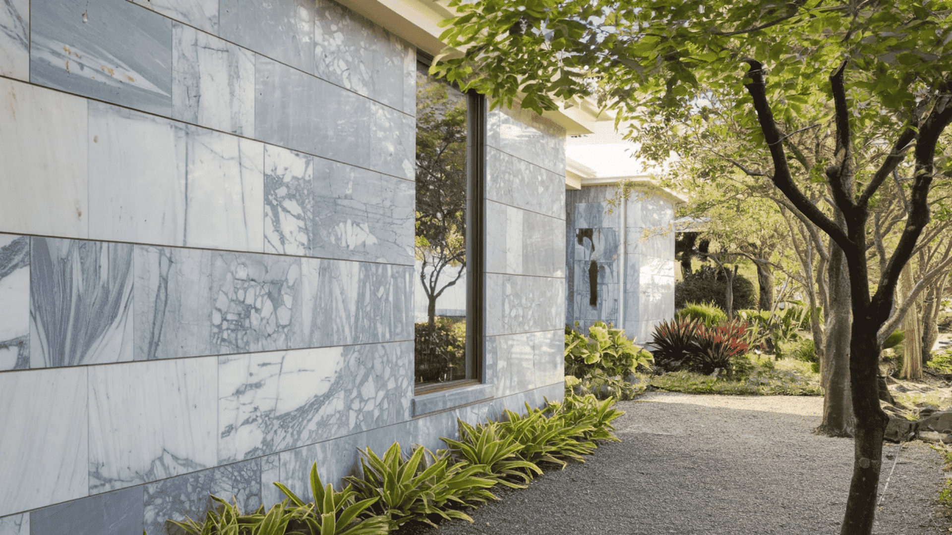 A lush walkway featuring trees and plants in front of a welcoming house