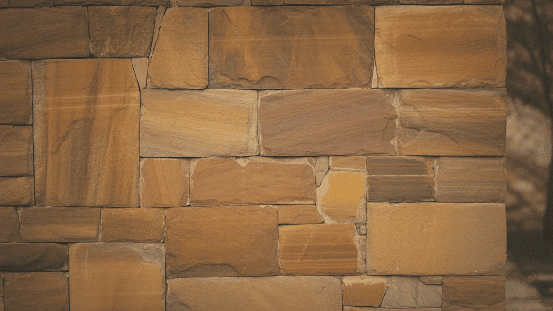 A textured stone wall featuring a pattern of brown and tan bricks arranged in a cohesive design
