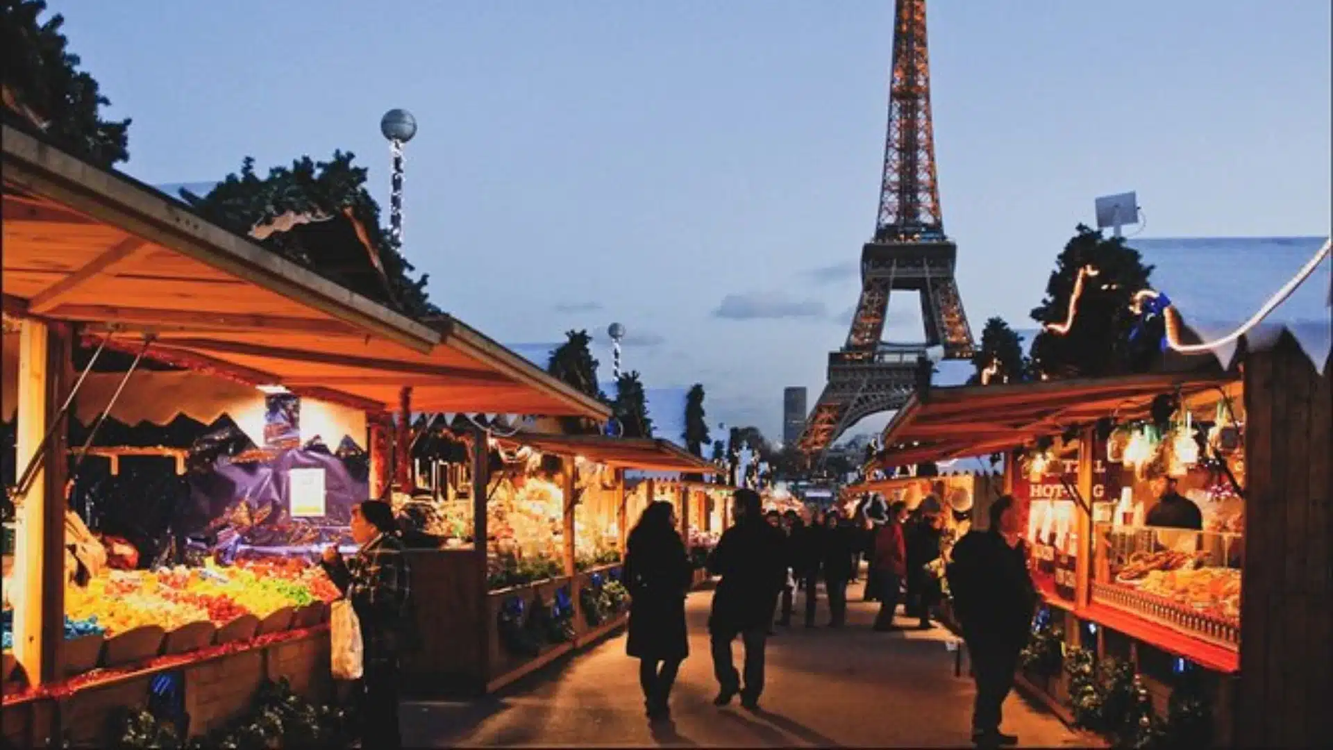 Bustling Les Puces de Saint-Ouen market at dusk, with illuminated stalls and the Eiffel Tower rising in the Paris skyline
