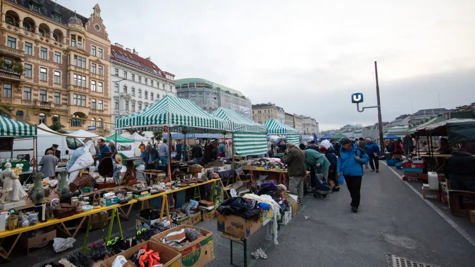 Flea market at Vienna Naschmarkt with striped stalls, vintage goods, and shoppers browsing along a city street
