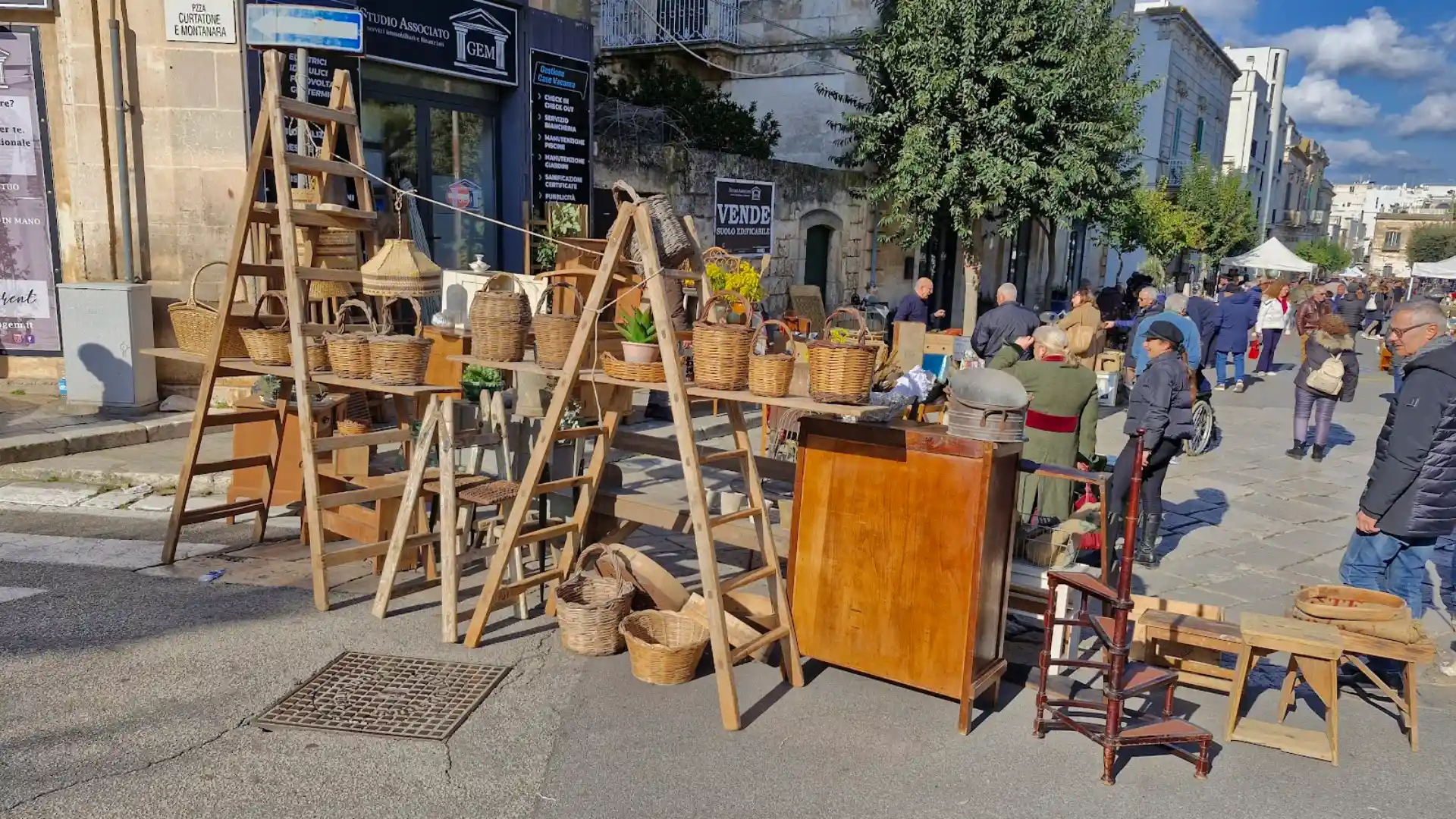 Ostuni antique market in Puglia with wicker baskets, wooden furniture, and shoppers browsing sunlit street stalls