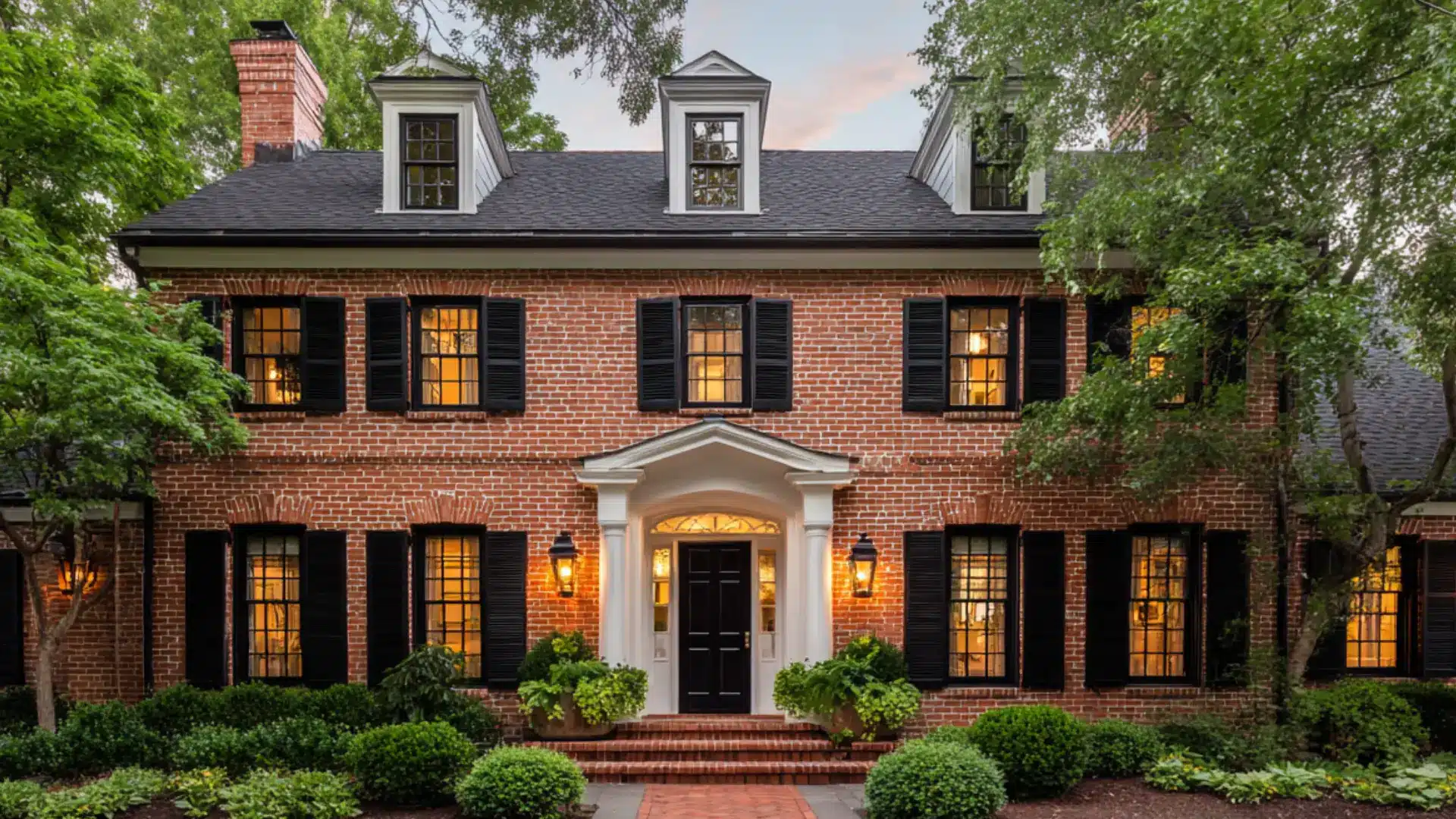 Classic red brick colonial house with black shutters white window frames a black front door and a brick garden walkway