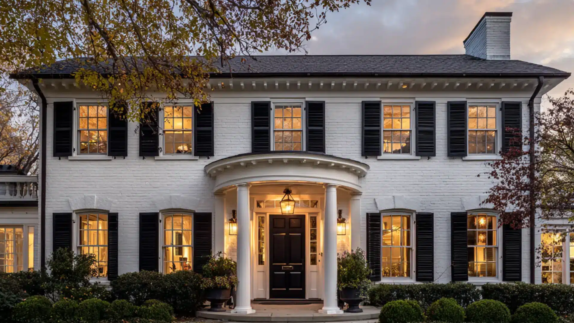 Colonial white brick house with shutters white columns on a large front porch with rocking chairs and green shrubs