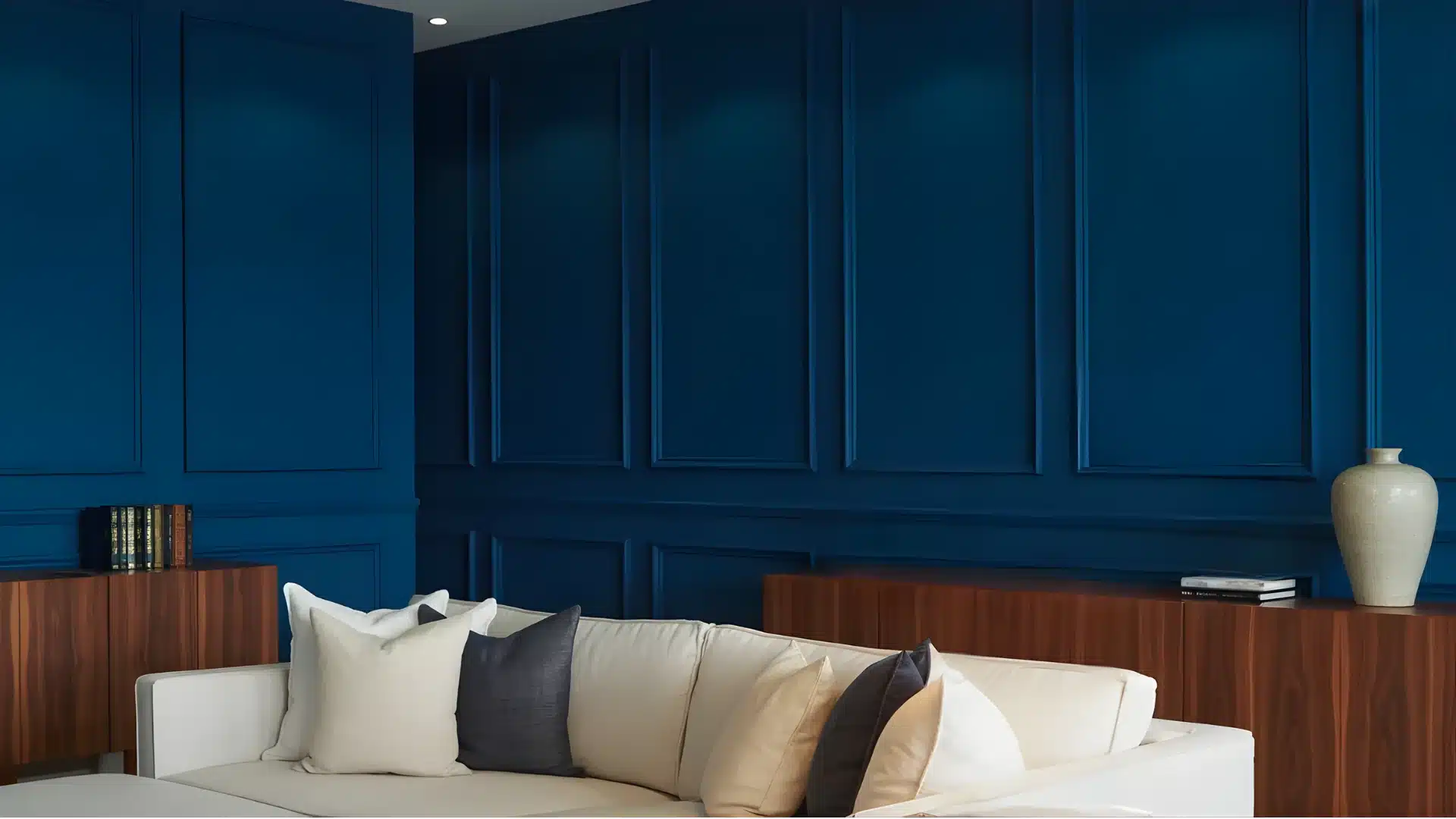 A luxurious living room corner features a white sectional sofa against deep indigo blue paneled walls, complemented by dark wood sideboards and neutral throw pillows