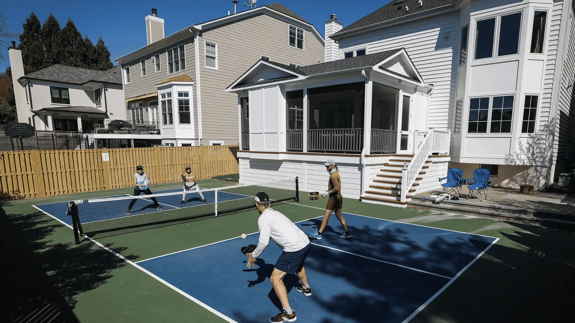 Friends playing pickleball on a backyard court beside a large suburban family home