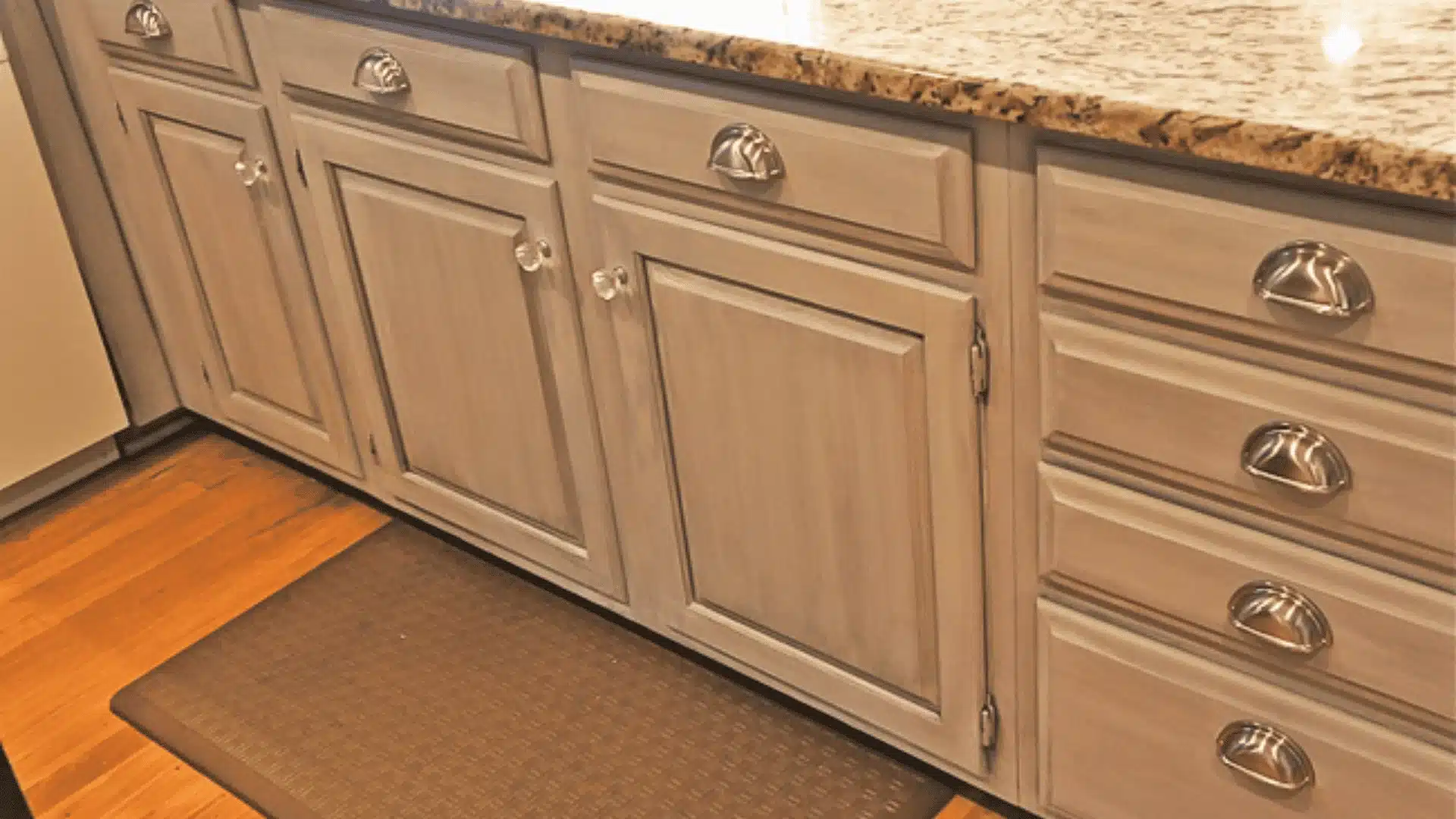 Grey glazed kitchen base cabinets with granite countertops, silver cup pulls, and clear knobs