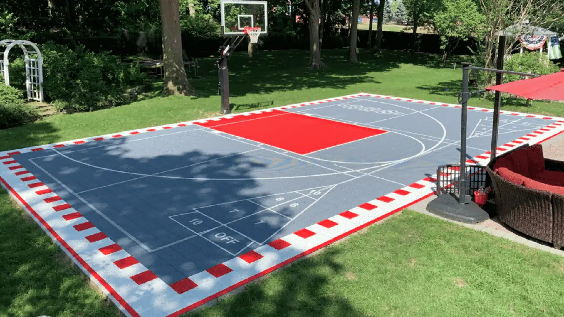 Backyard multi game court with red and gray tiles surrounded by lush green landscaping
