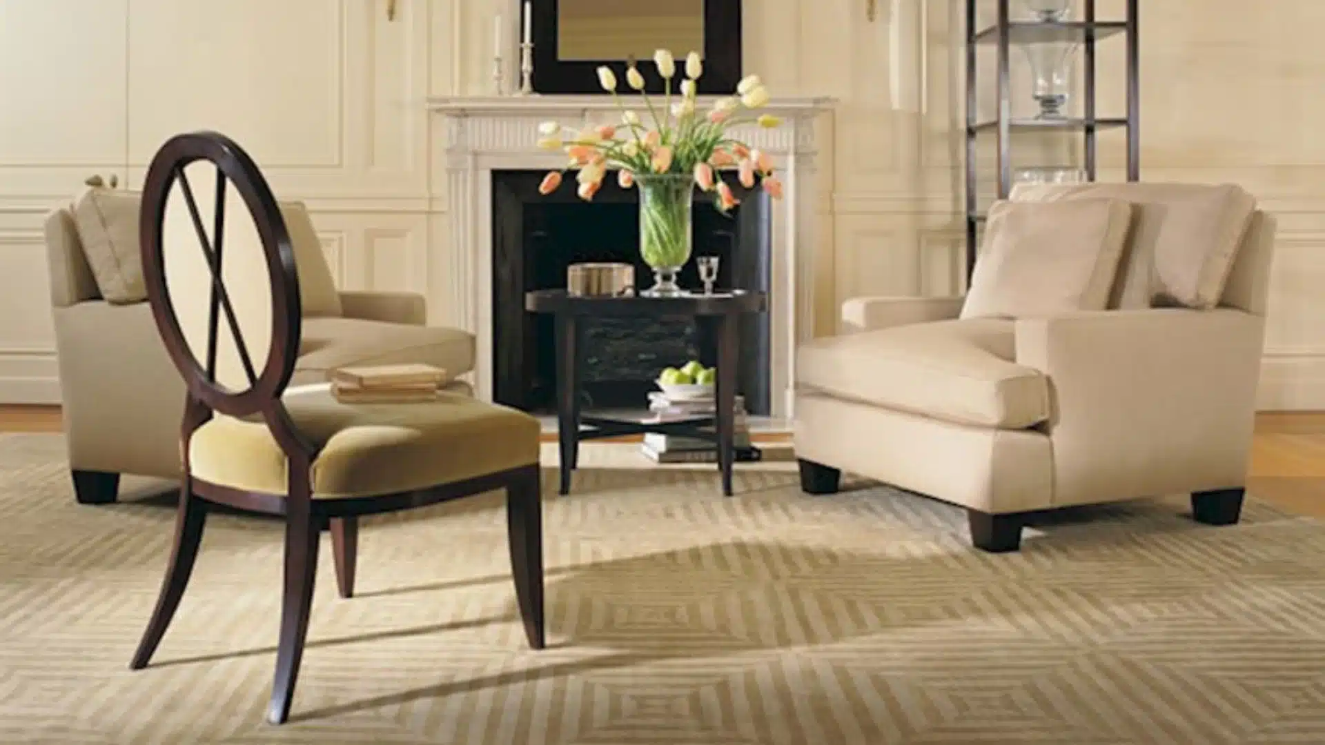 Elegant living room with cream armchairs, a dark wood accent chair and side table, fireplace, flowers, and a neutral patterned rug.