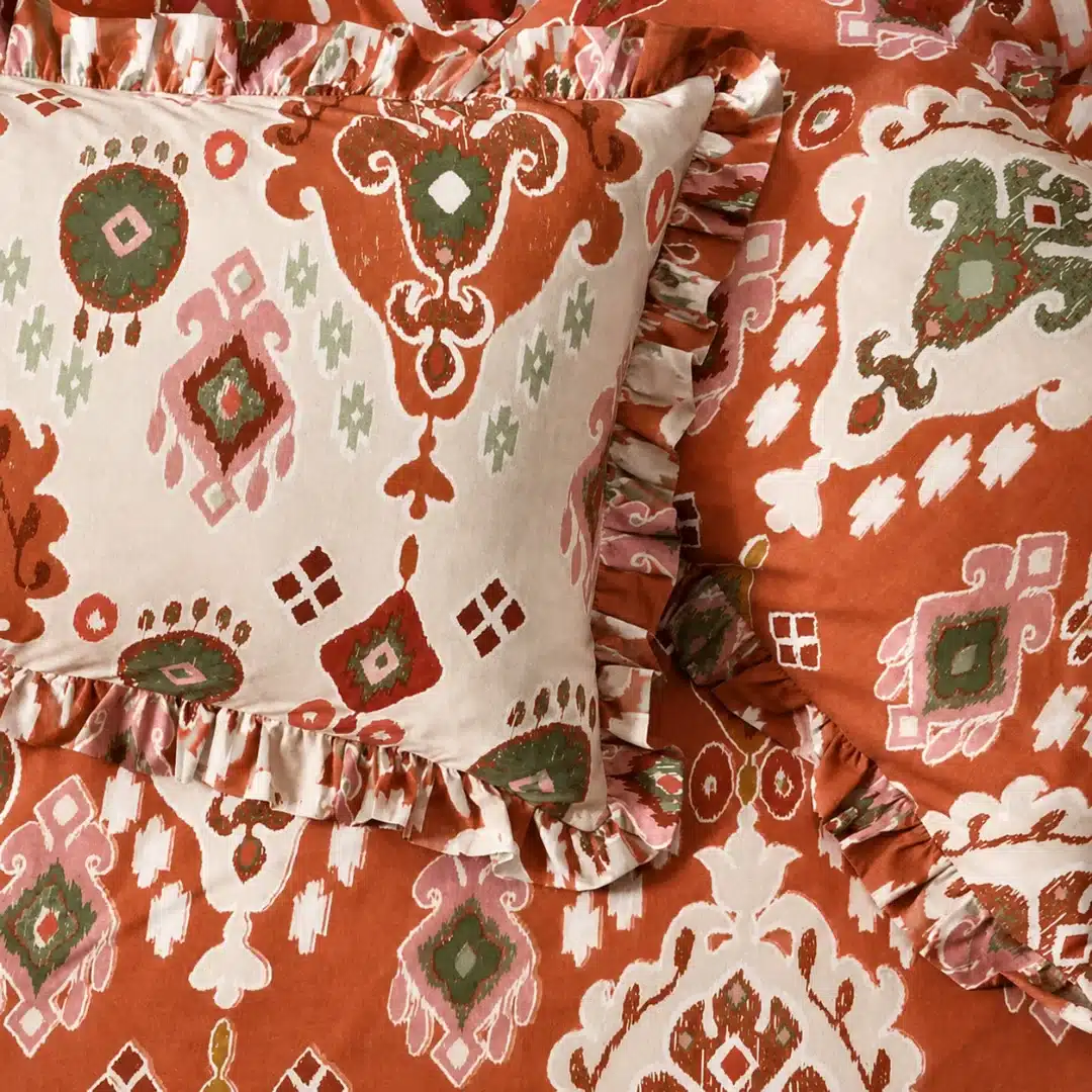 Burnt orange and sage green patterned bedding with ruffled pillows