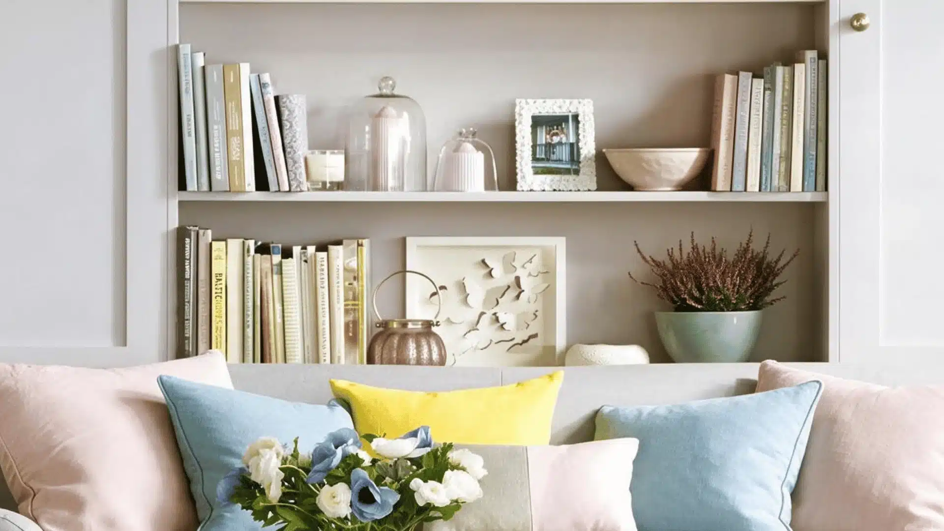 Soft gray shelves behind a colorful couch with books, photos, and plants.
