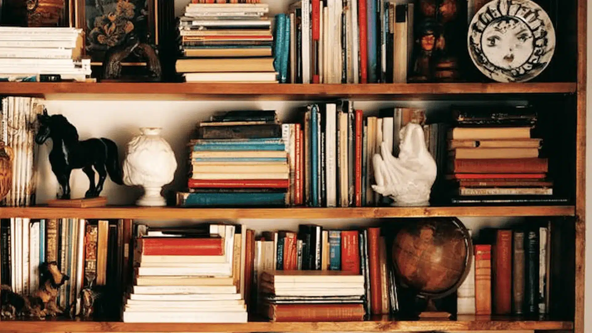 Wooden bookshelf packed with stacked books, figurines, a globe, and trinkets.