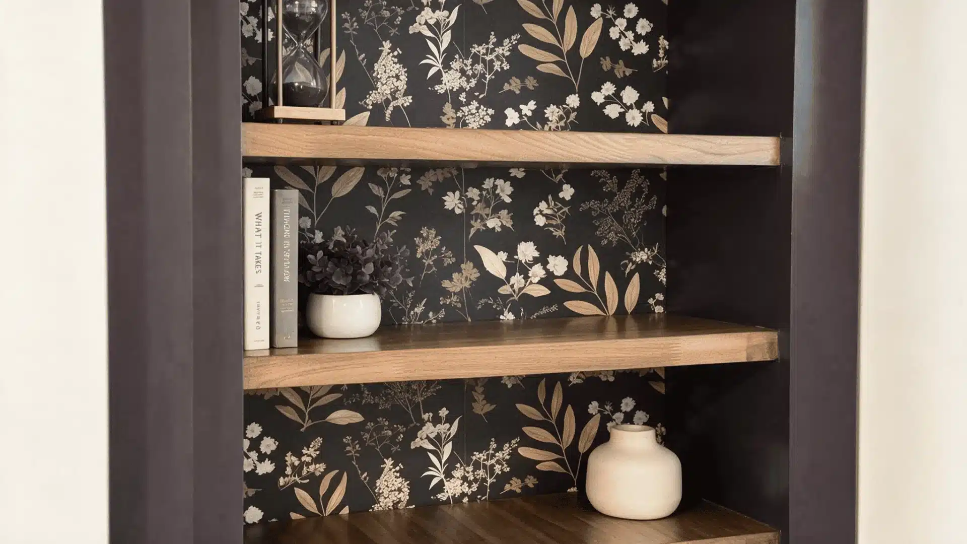 Wooden bookshelf with dark floral backing, books, small plant, and decor