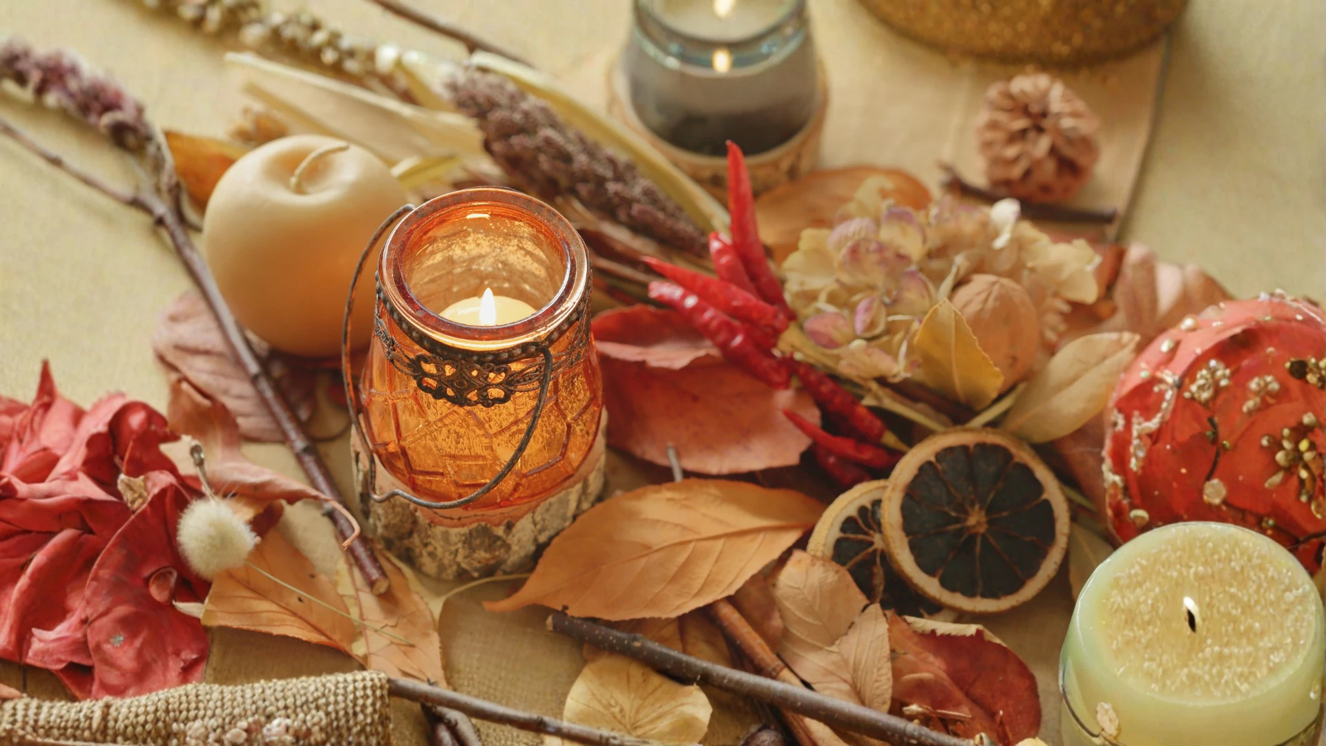 Autumn centerpiece with lit candles, dried leaves, citrus slices, and red peppers.
