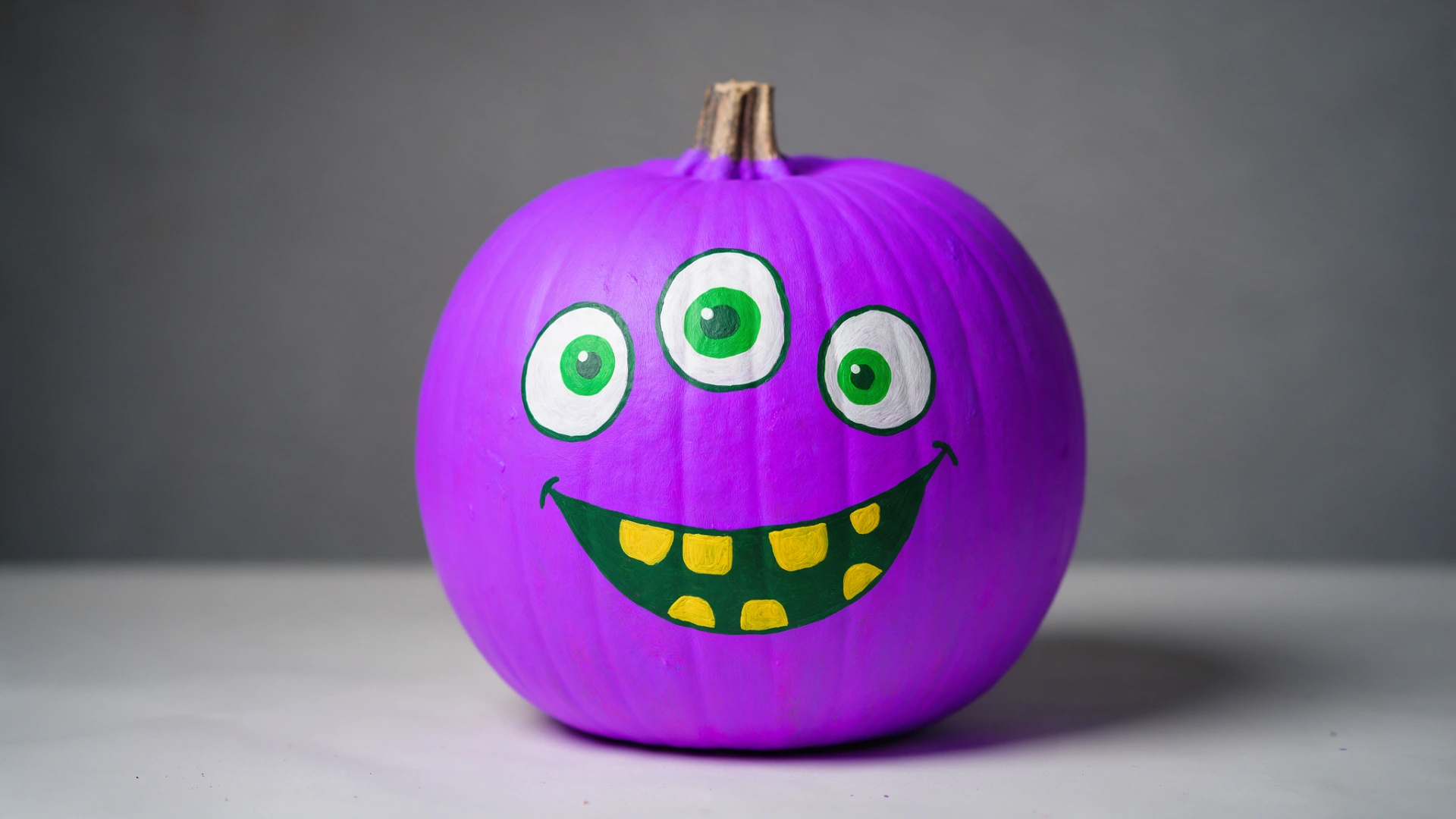 Bright purple pumpkin painted with a playful, three-eyed green mons