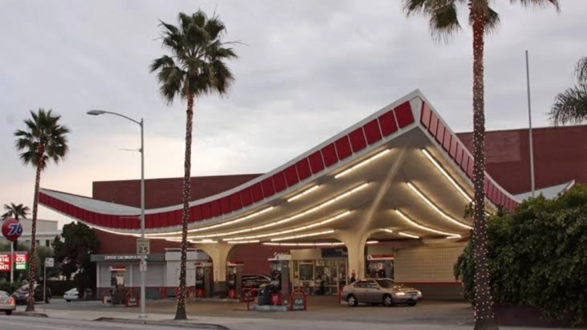 Googie gas station with sweeping red canopy bright lights palm trees and classic roadside architecture.