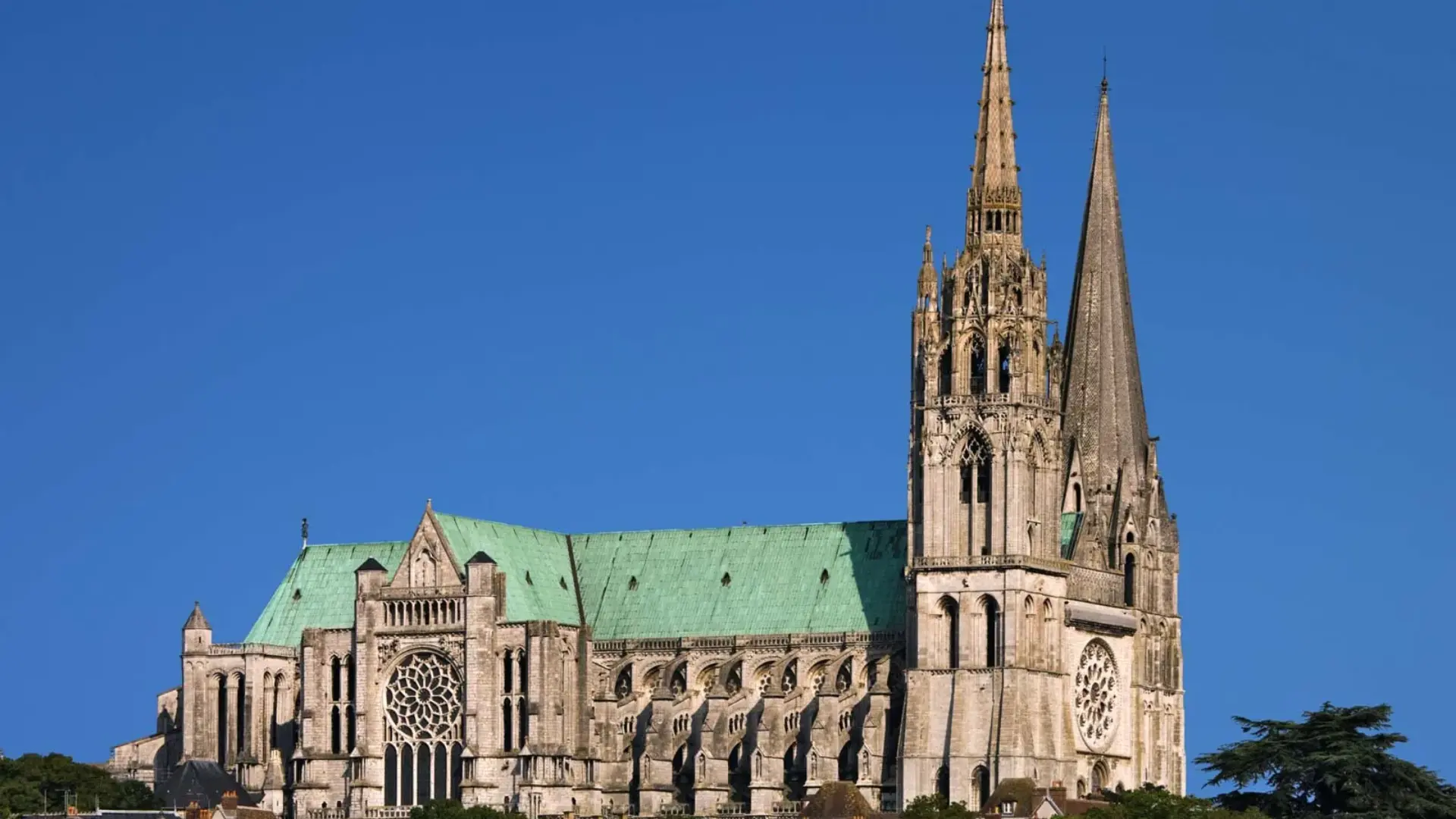 Gothic cathedral with pointed arches, a large rose window, and two tall spires against a clear blue sky.