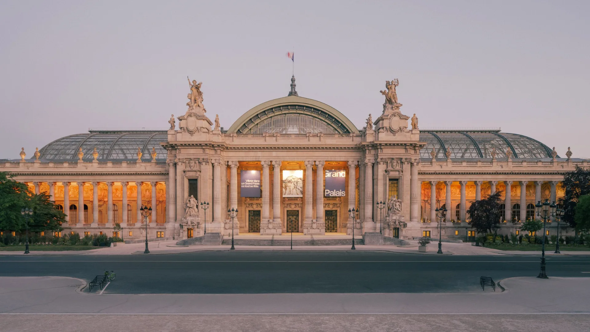 Grand Palais in Paris with symmetrical stone facade tall columns glass roof sculptures and warm evening lights