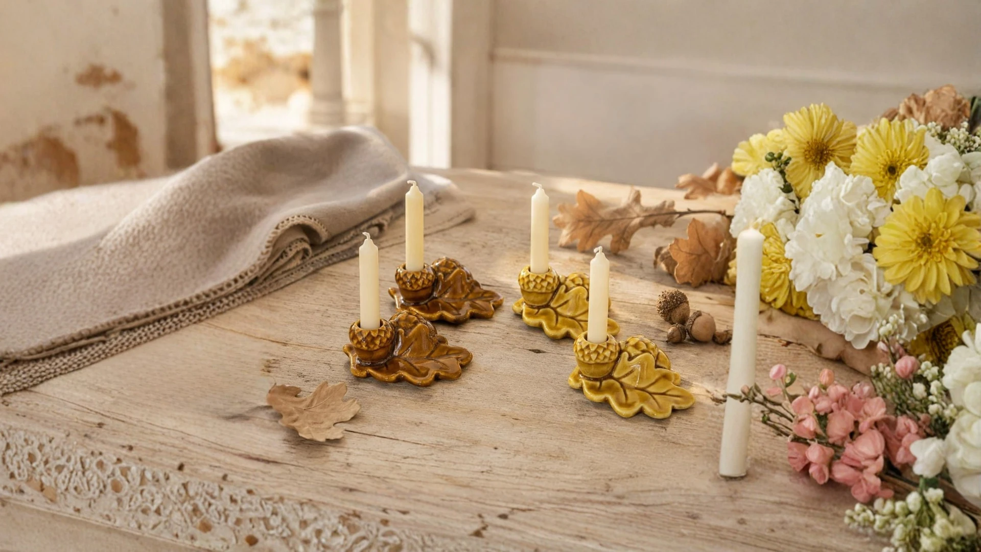 Leaf and acorn-shaped ceramic candle holders on a wooden table with flowers.