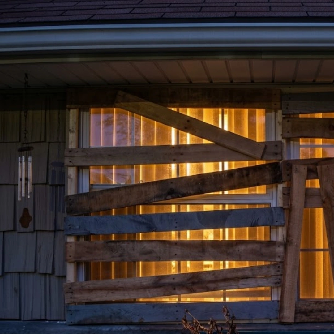 Wooden pallets board up a house window and doorway, with warm indoor light glowing through for a spooky abandoned Halloween look.
