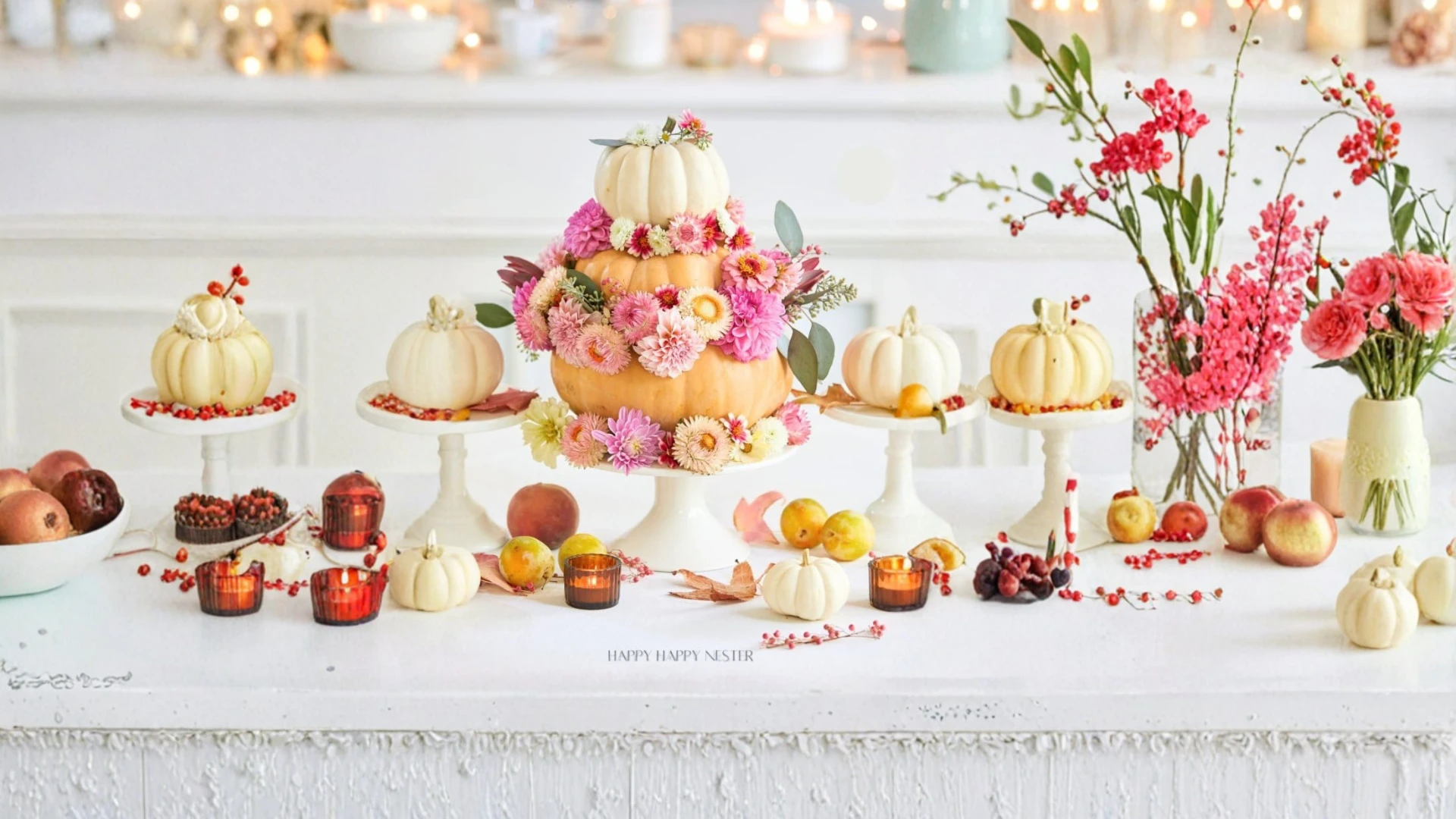 Tiered pumpkin and pink flower display surrounded by white pumpkins and fruit.