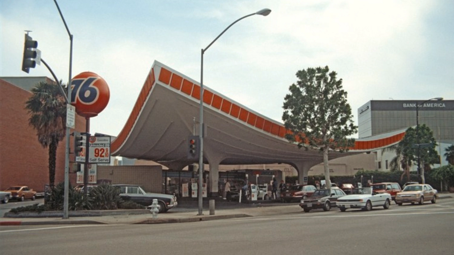 Vintage Googie gas station with sweeping canopy bold orange trim roadside signs and classic cars.