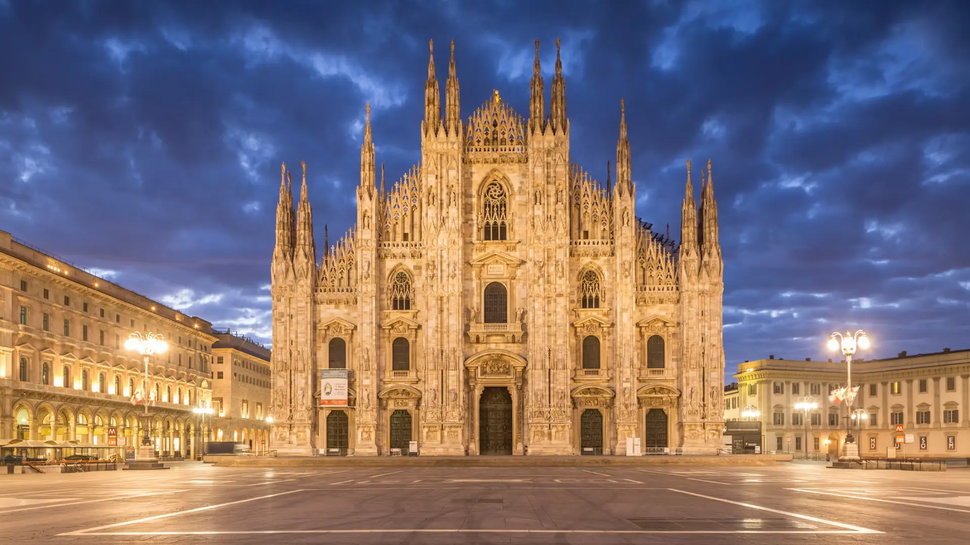 Late Gothic cathedral with ornate spires and pointed arches illuminated at dusk in a city square.