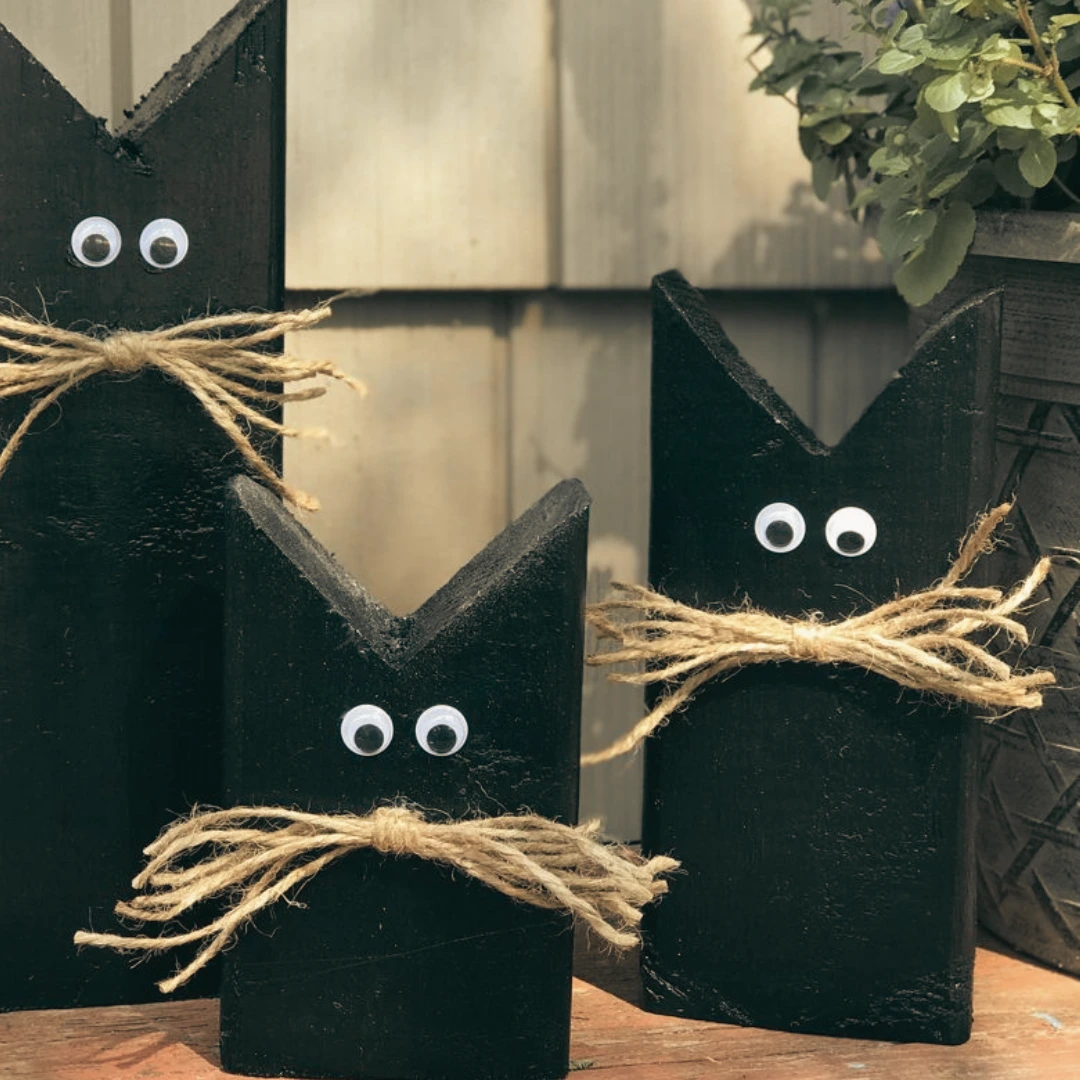 Three black wooden cat decorations with googly eyes and twine whiskers displayed outdoors as simple Halloween porch decor.