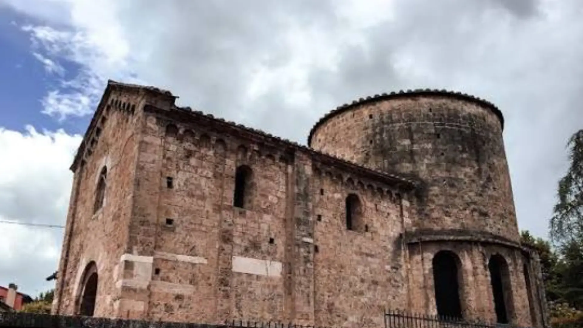 Pre-Romanesque brick building with a rounded apse and arched windows under a cloudy sky