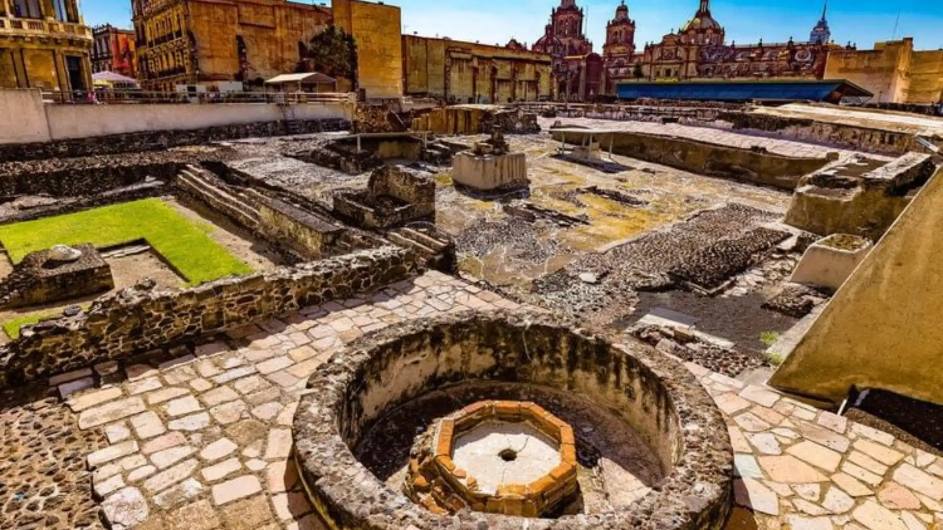 Templo Mayor archaeological site in Mexico City with ancient stone ruins and historic buildings in the background.