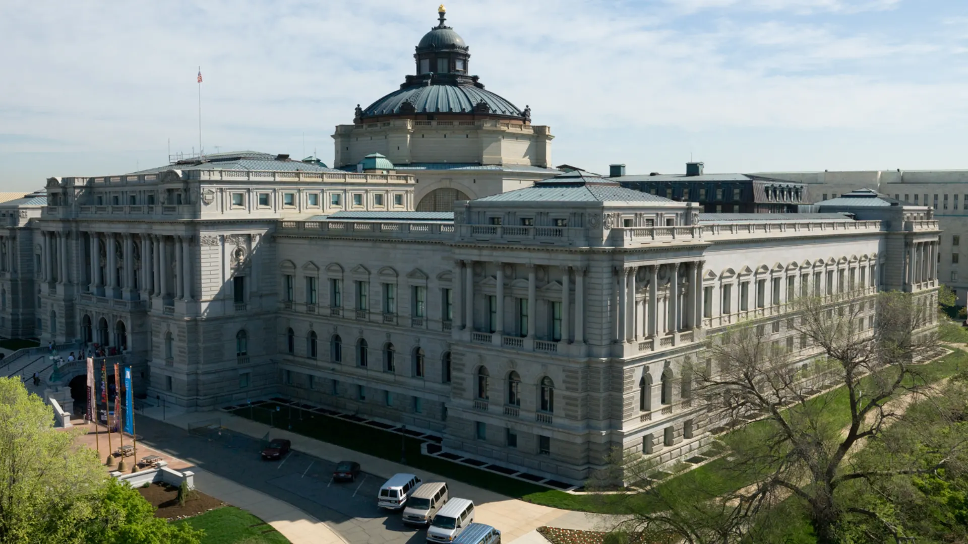 Large Beaux Arts civic building seen from a corner with stone walls, arched windows, classical columns, and formal grounds
