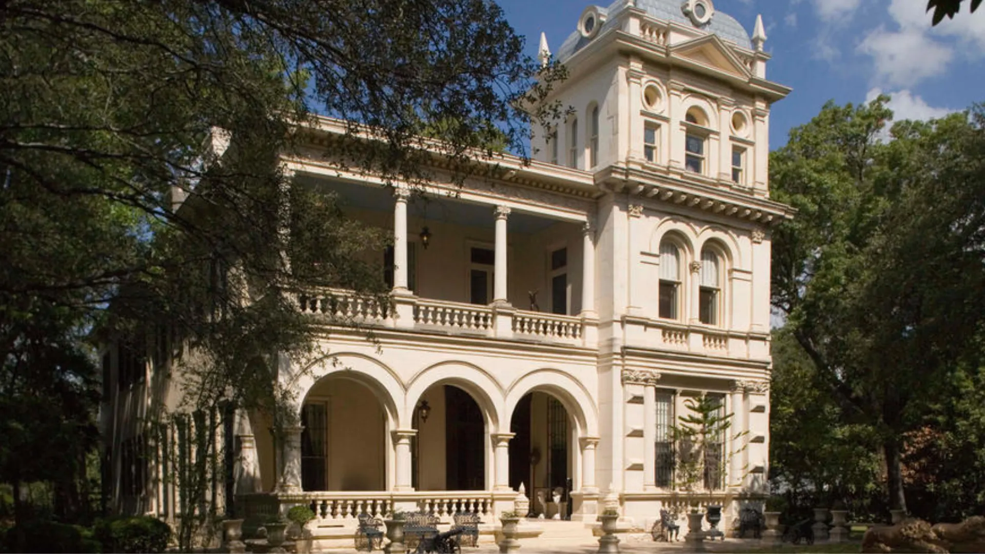 Elegant Italianate villa with arched porch tall tower ornate windows decorative roofline and leafy garden setting
