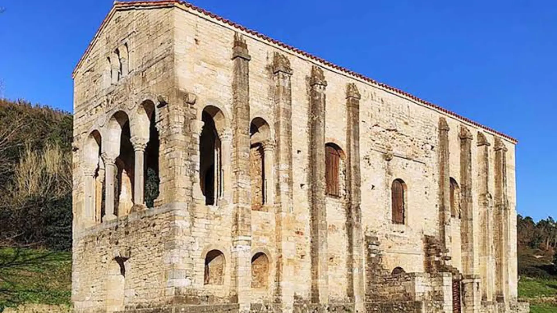 Medieval stone building with arched openings and tall exterior columns under a clear blue sky