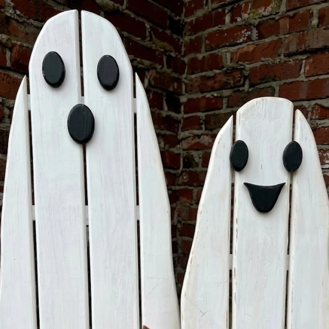 Two white wooden pallet ghosts with black facial features stand against a rustic red brick wall as simple outdoor Halloween decor.